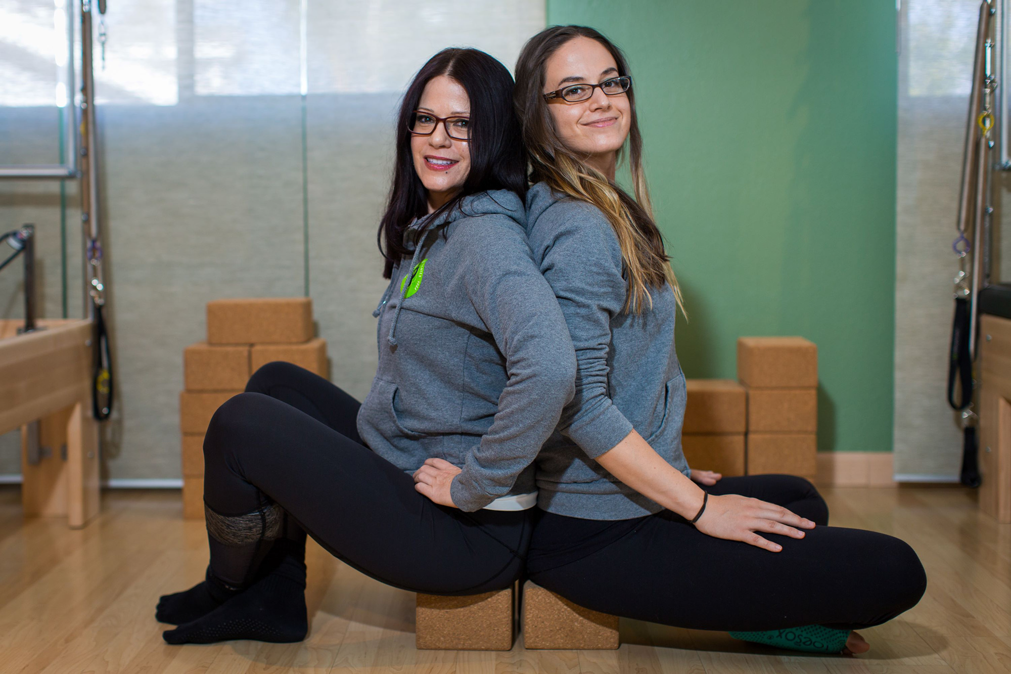 Denise and Kelly, mother–daughter owners of Fit Monkeys, sitting back to back in the studio.